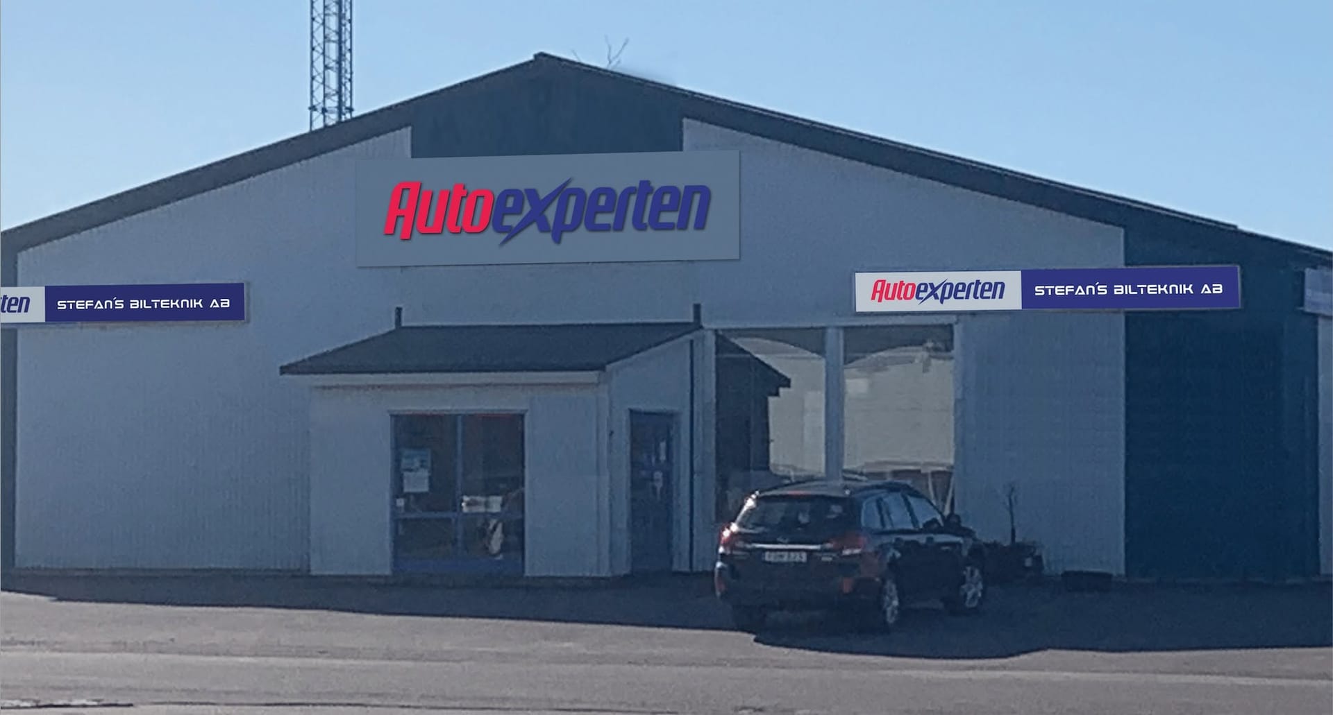 Verkstadsbyggnaden dagtid med en mörk SUV utanför porten